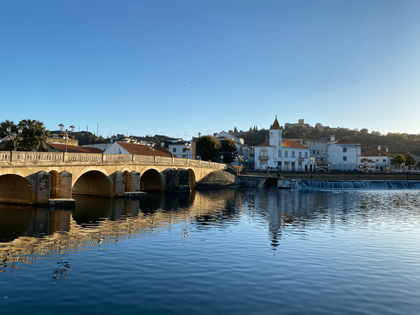 Historic bridge over the Nabão River, with a view of Tomar Castle in the background.