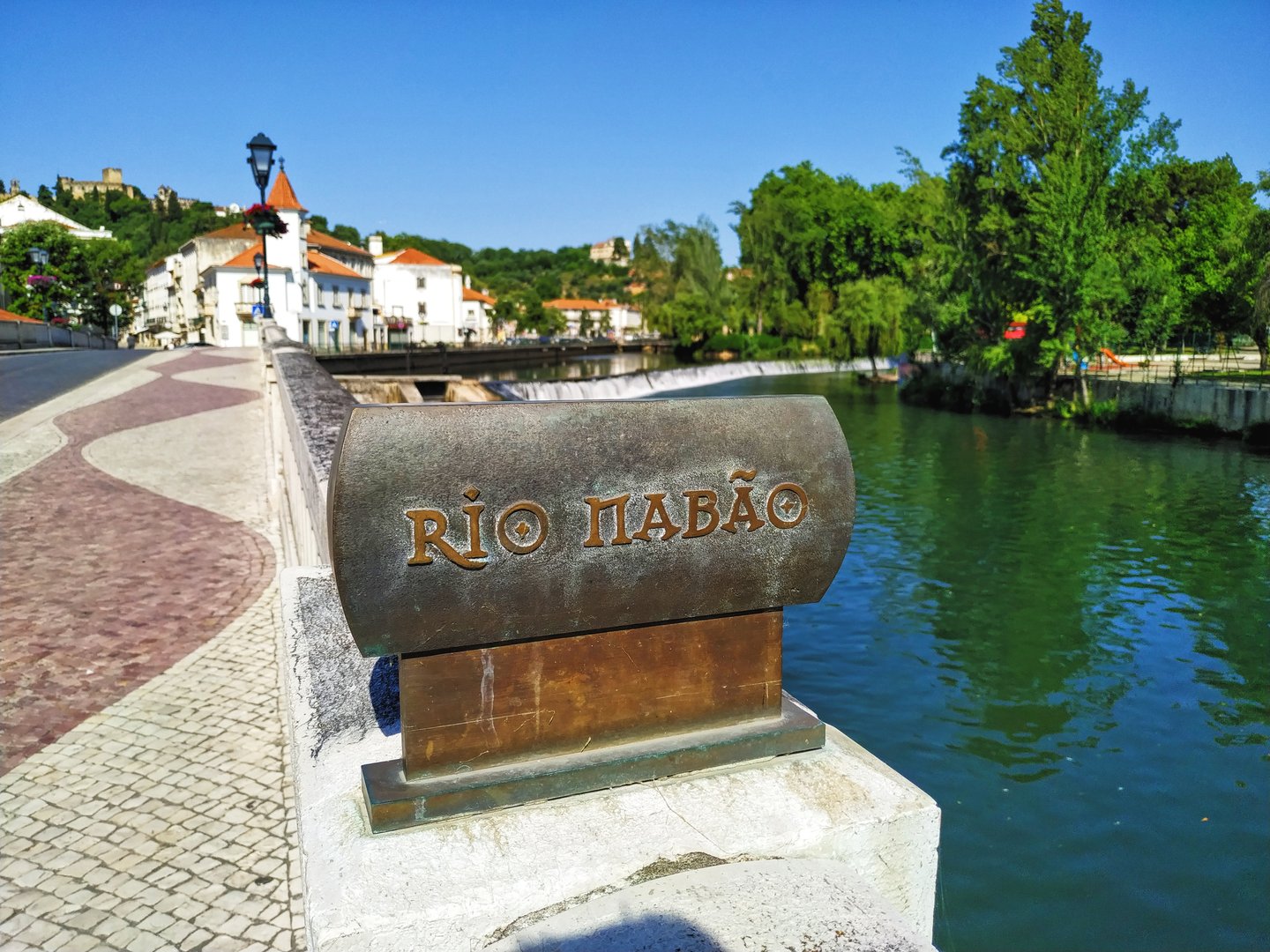 Sign on the Nabão River, highlighting the river's name with Tomar Castle in the background.